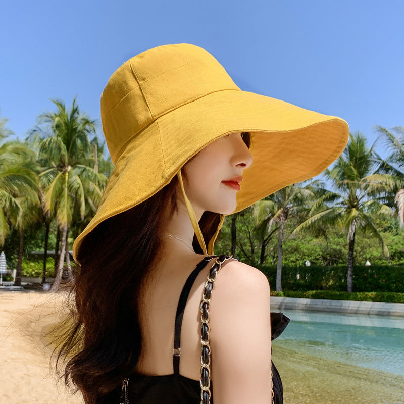 Japanese solid color big brim fisherman's hat in yellow worn by a woman at the beach.