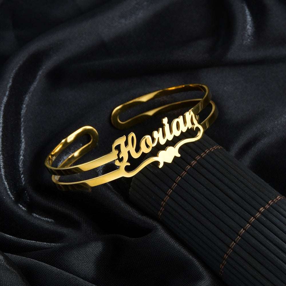 Gold customized name bracelet on black fabric background, personalized stainless steel bangle.