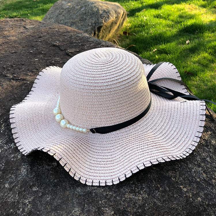Women's straw hat with big brim, monochrome design, adorned with a bow and pearl detail, perfect for summer.