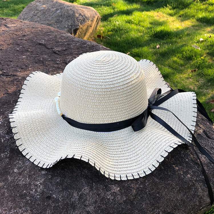 Women's straw hat with big brim and black bow, woven in warp knitting, ideal for summer.