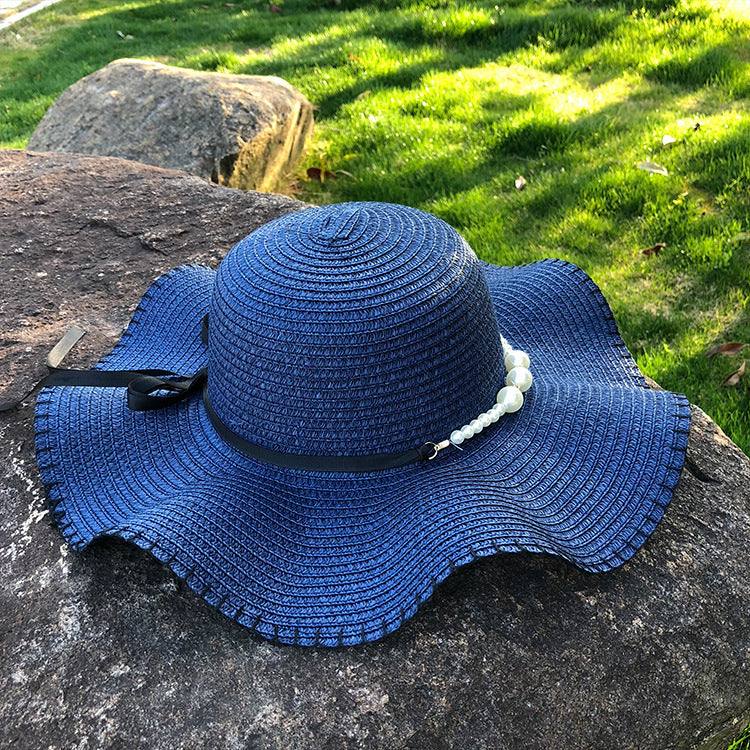 Women's straw hat with big brim in navy blue on a rock, featuring a bow and pearl embellishment for a summer look.