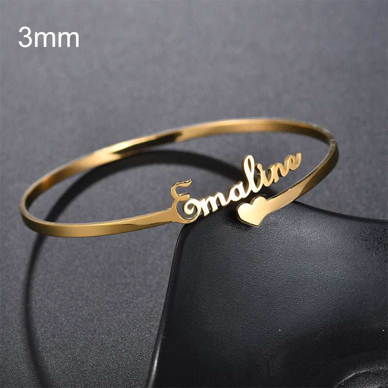 Customized name bracelet in gold with "Emaline" script design and heart accent, made of stainless steel.