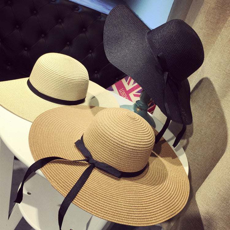 Women's straw woven big brim sun hat in khaki, beige, and black colors on table.