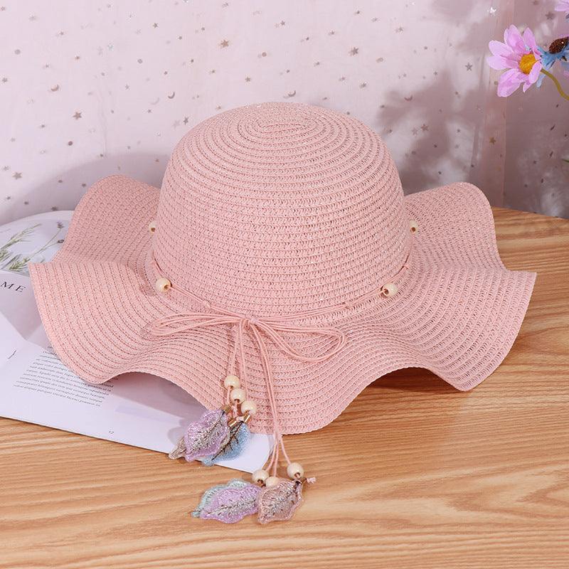 Ladies big brim wave straw hat in pink with dome style and bow detail, placed on a table.