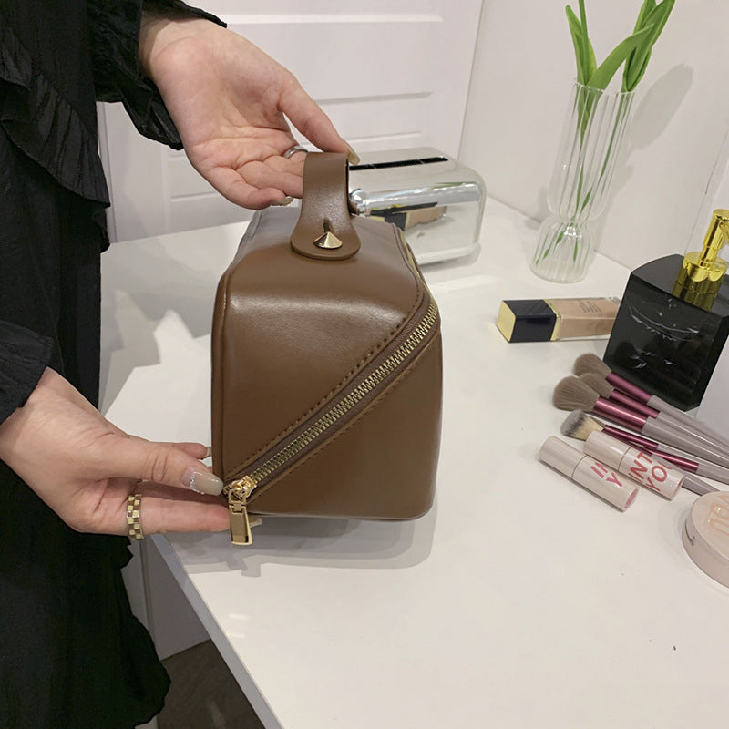 Cosmetic bag in brown PU leather with gold zipper on a dressing table with makeup items.
