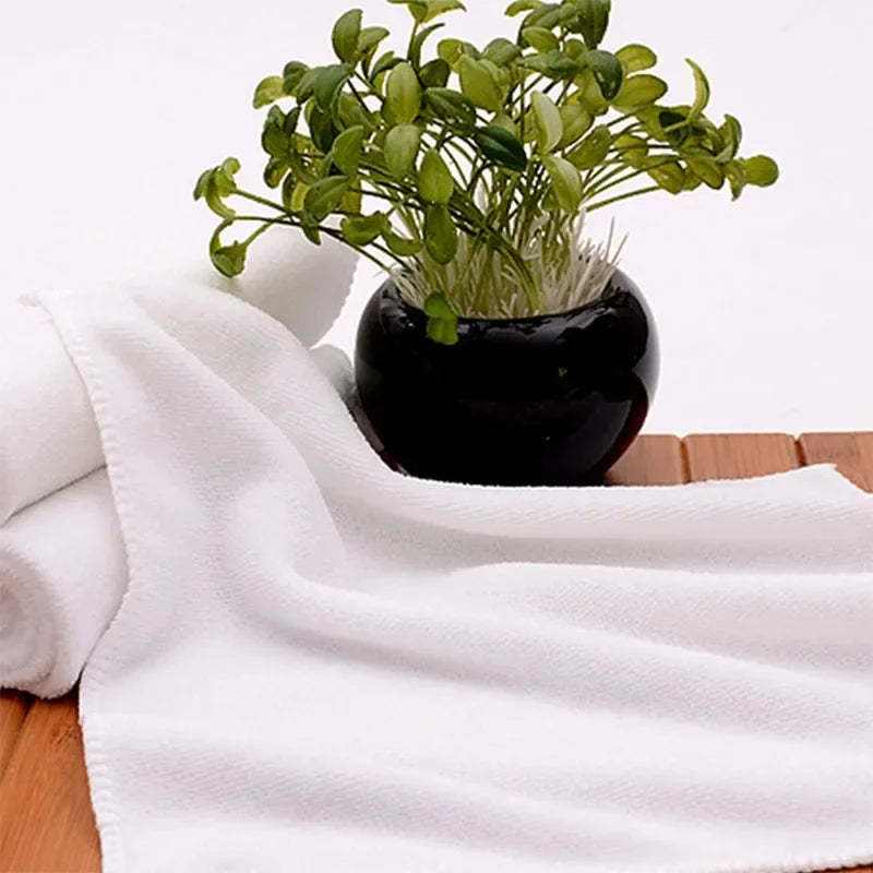 Absorbent thickened microfiber white towel for hotel use on a wooden surface with a plant nearby.