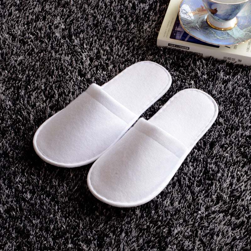 White disposable hotel slippers on carpet for guest rooms.
