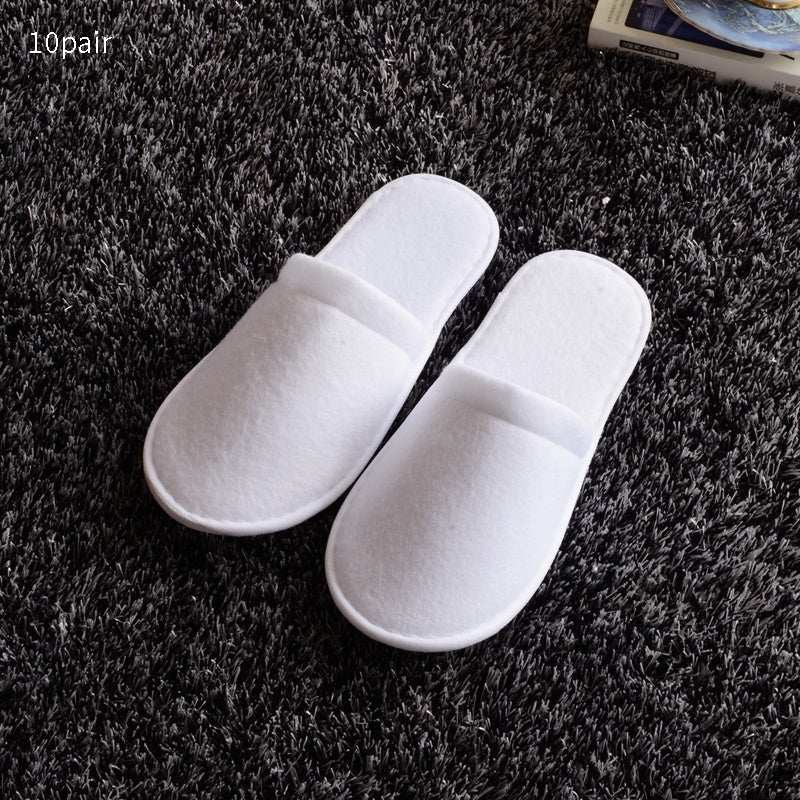 White hotel slippers on a dark carpet, disposable and free size.