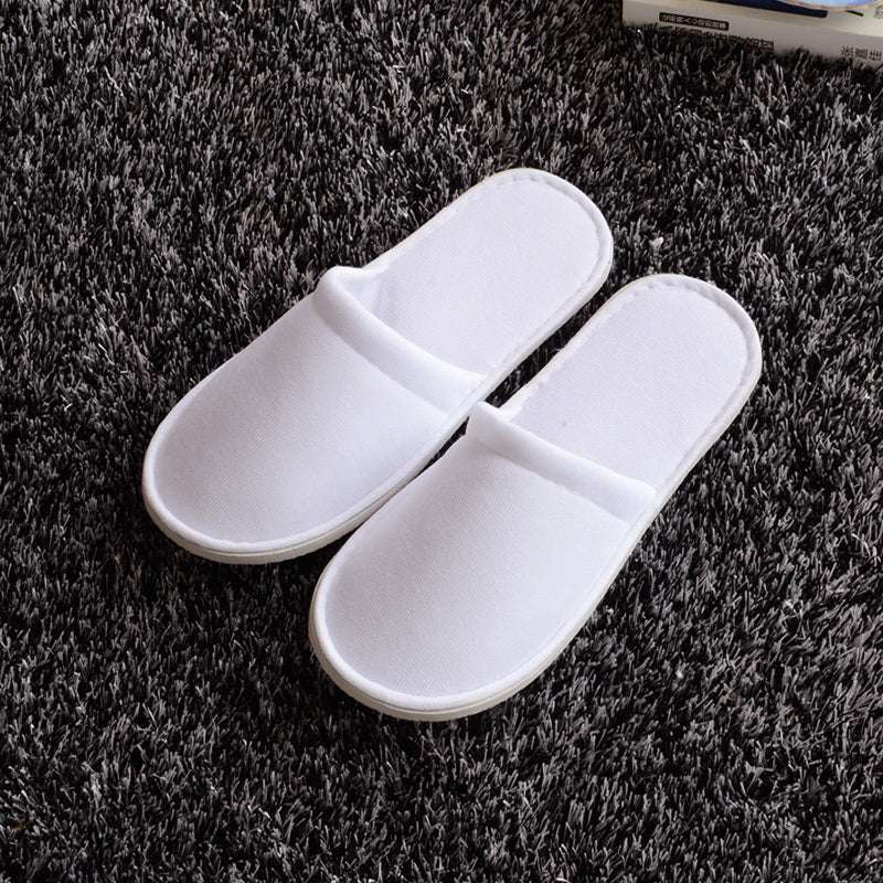 White disposable hotel slippers on a dark carpet, designed for couples, free size, suitable for spring and autumn.