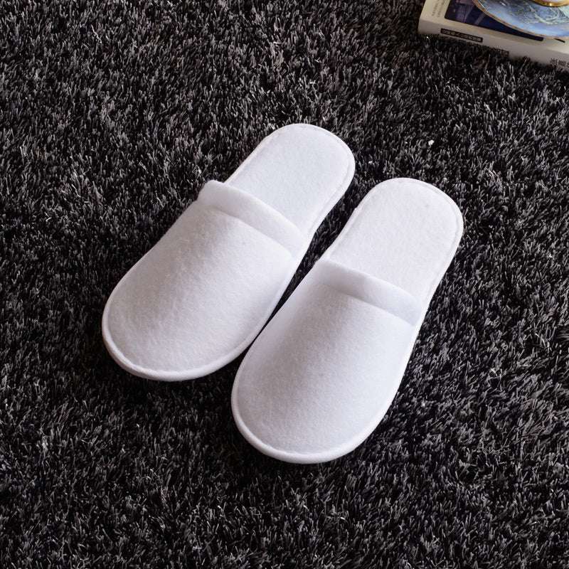 White disposable hotel slippers on a dark carpet surface.