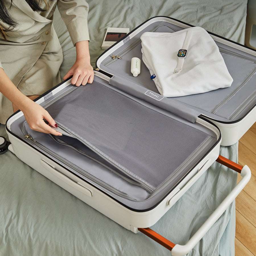 Wide trolley case with open compartment showing zipper bags, on a bed, features large capacity.