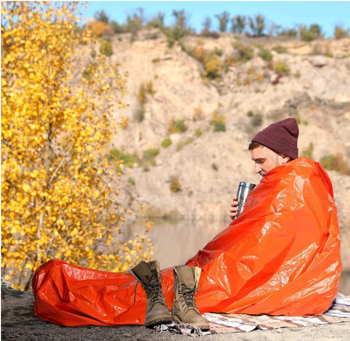 Orange first aid sleeping bag in outdoor setting with person staying warm.