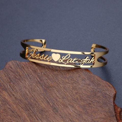 Customized gold name bracelet with heart detail on wooden surface.