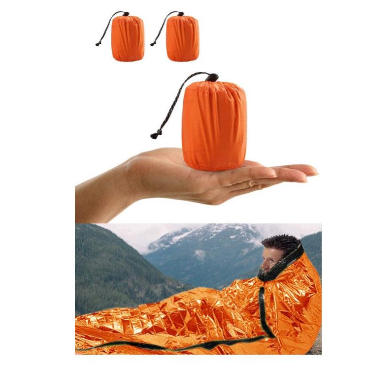 Orange first aid sleeping bag thermal blanket, compact size in hand and in use outdoors.