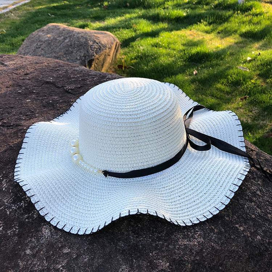 Women's straw hat with big brim and black bow, featuring a dome top and wavy edge, ideal for summer.