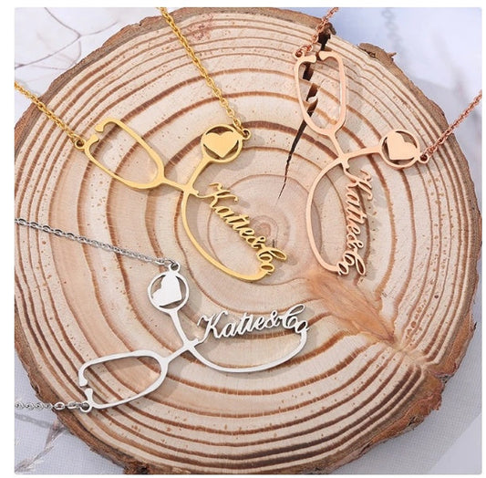 Customized stainless steel stethoscope name necklaces in gold, rose gold, and silver on a wooden background.