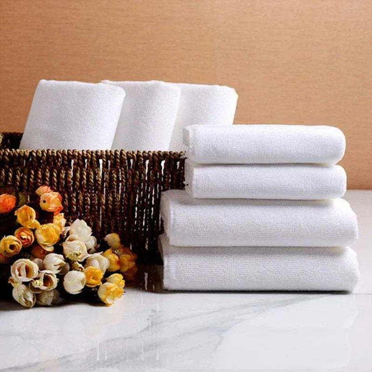 White microfiber towels stacked near a basket and flowers, ideal for hotel room cleaning.
