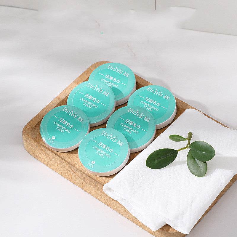 Disposable compression towels on a wooden tray with a green leaf, showcasing compact design and travel-friendly features.