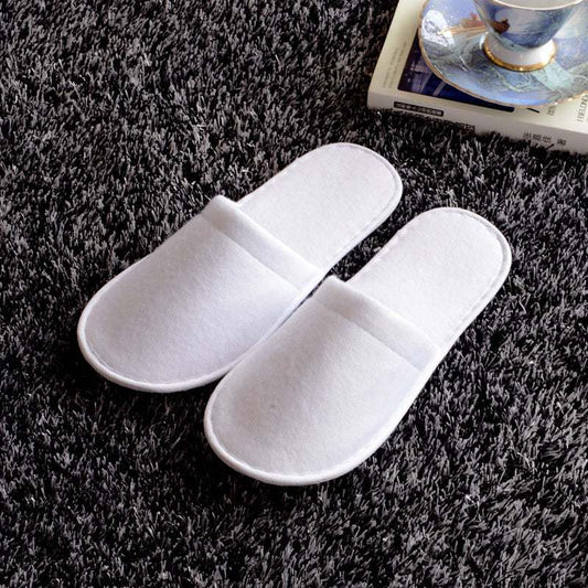 White disposable hotel slippers on carpet for guest rooms.