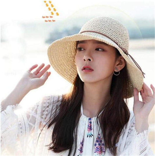 Foldable raffia women's big brim beach hat in beige on woman at seaside.